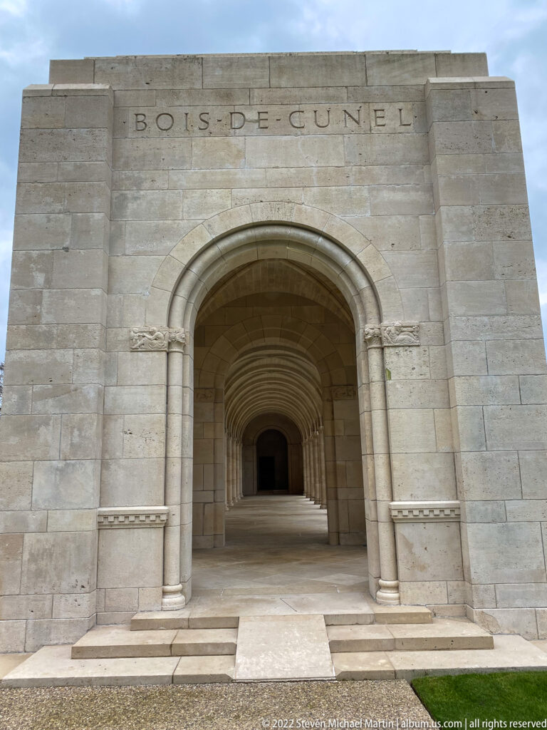 Long stone arcade of repeating round arches recedes into a dark passage beneath a carved place-name inscription.