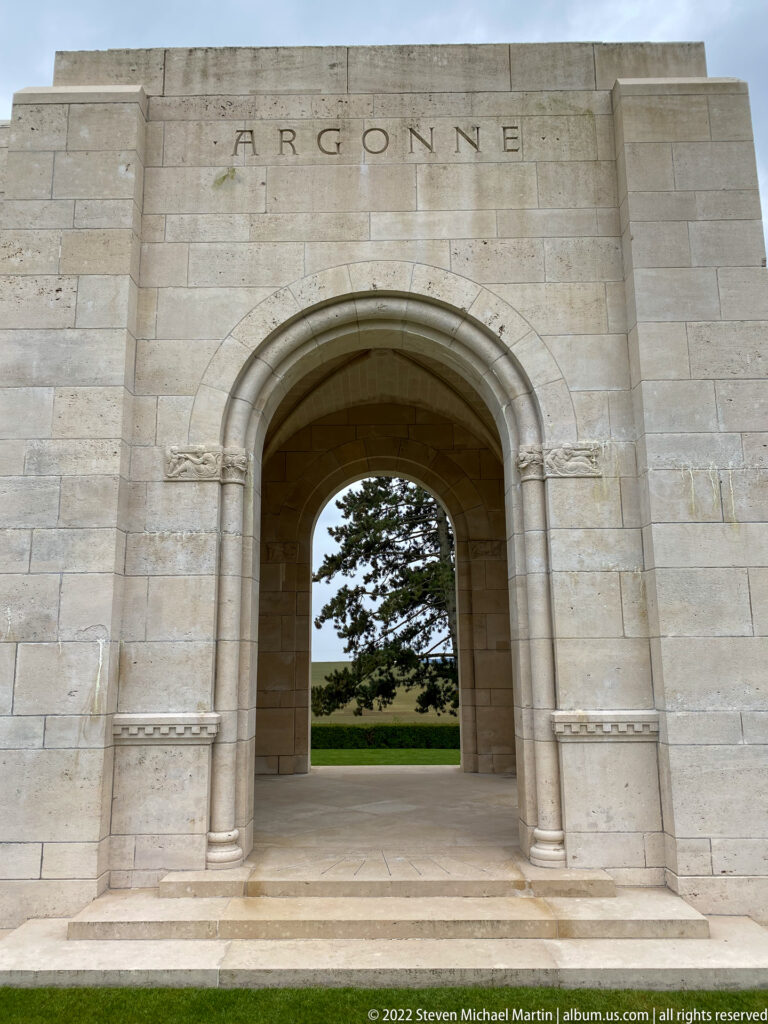 Large stone arch inscribed ARGONNE frames a mature tree and green lawn outside.