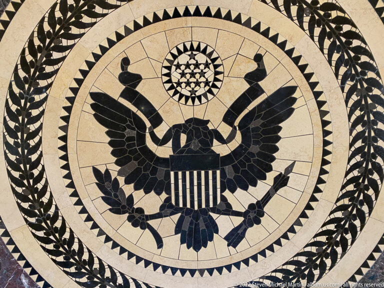 Circular mosaic of the American eagle with shield, olive branch, arrows, stars, and leafy border.