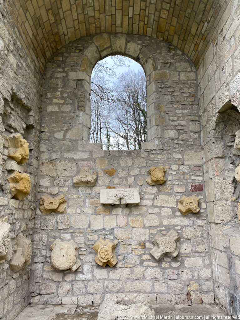 Carved stone fragments are embedded across a rough masonry wall beneath a large arched opening.