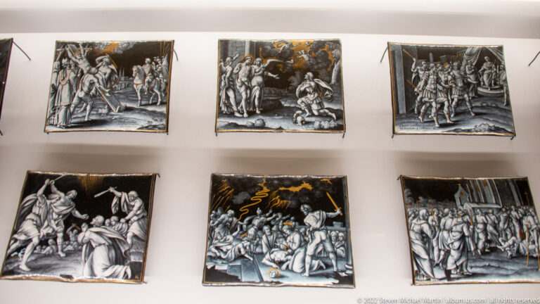 Six dark narrative enamel plaques arranged in two rows, each filled with small figural scenes.