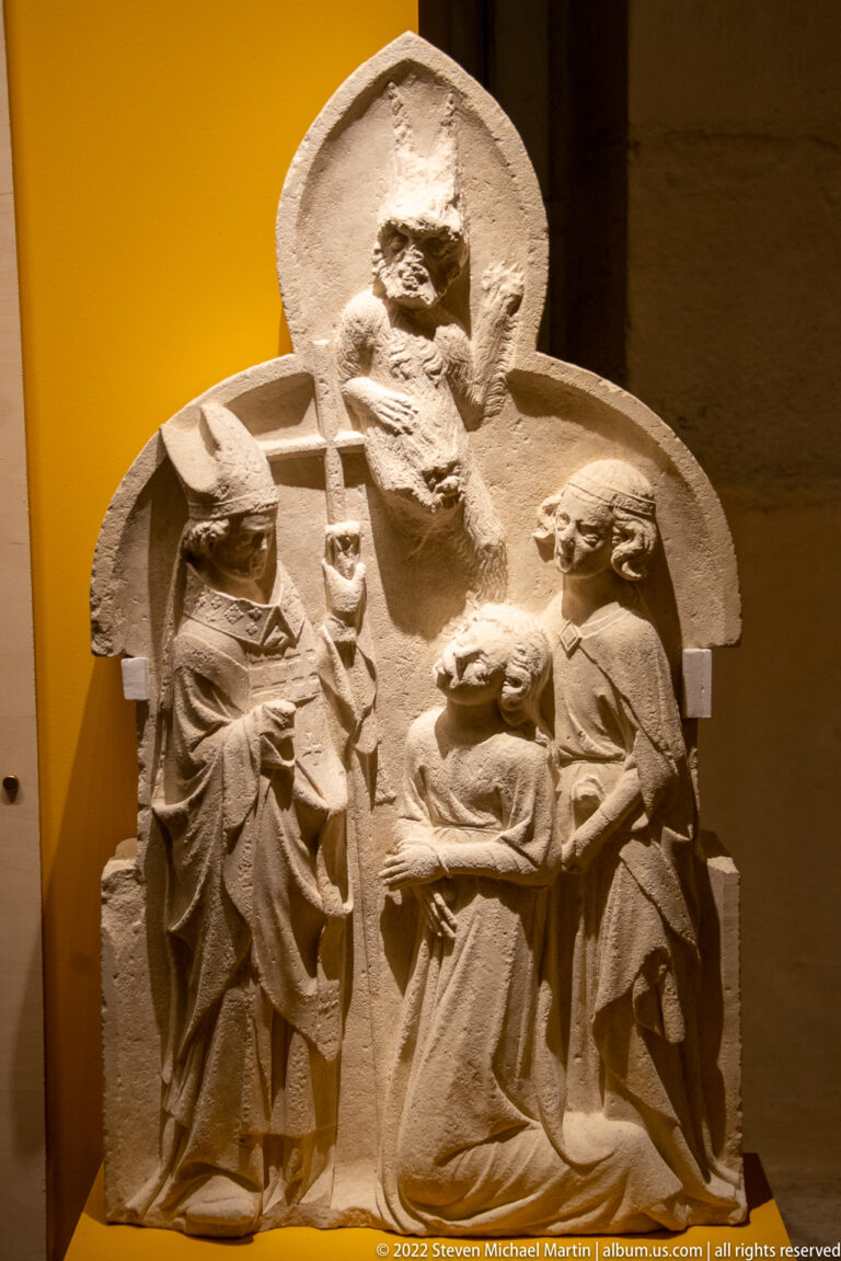 Stone relief of a large seated cleric or bishop flanked by two smaller ecclesiastical figures.