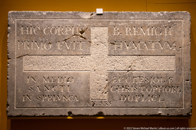 Rectangular inscribed stone slab with a large central cross and Latin text in four surrounding fields.