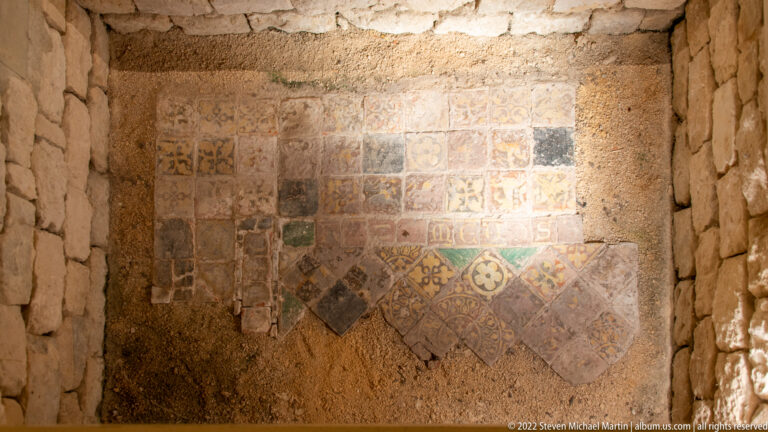 Fragmentary patterned tile pavement preserved against rough masonry, with square and diagonal decorated tiles.