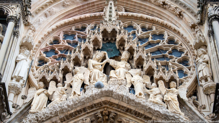 Gothic portal sculpture at Reims Cathedral showing Christ and the Virgin beneath a canopy, surrounded by angels and carved arches.