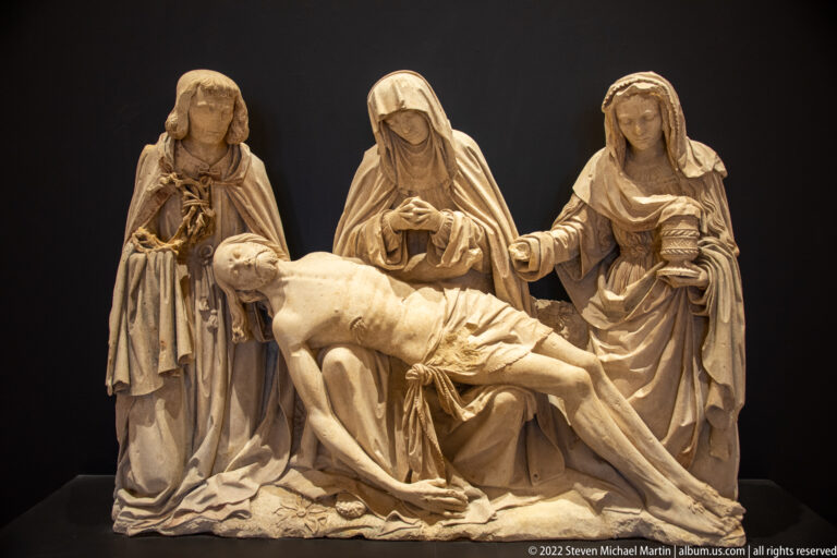 Four mourners surround and support the dead Christ in a pale stone Lamentation or Pietà group.