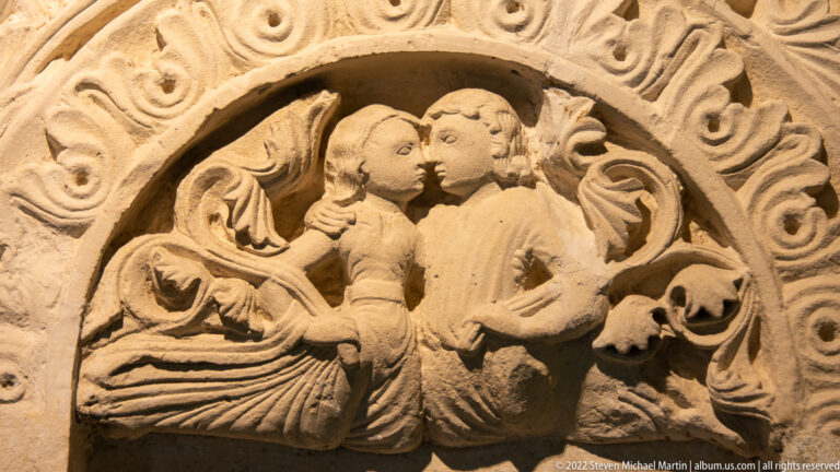 Two carved stone figures embrace or kiss within a circular frame of scrolling foliage.