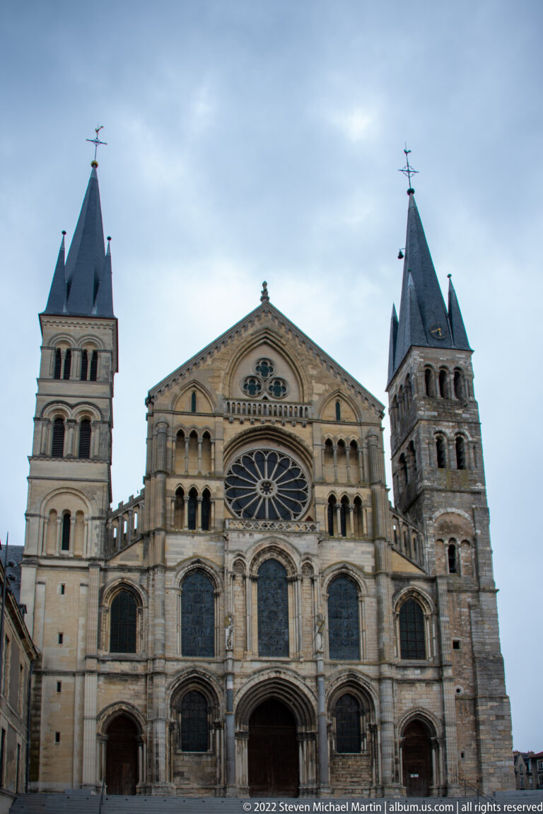 West façade of the Basilica of Saint-Remi with twin towers, central rose window, arcades, and three portals.