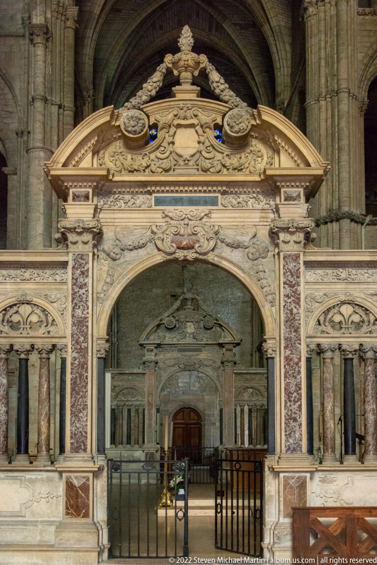 Ornate polychrome marble church monument with paired columns, carved pediment, red-veined panels, and central opening.