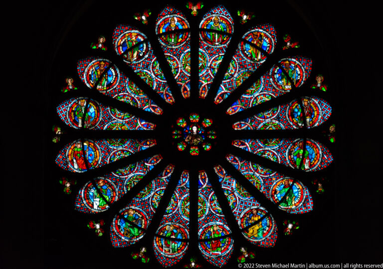 Multicolored rose window with long petal-shaped lobes radiating from a small floral center.