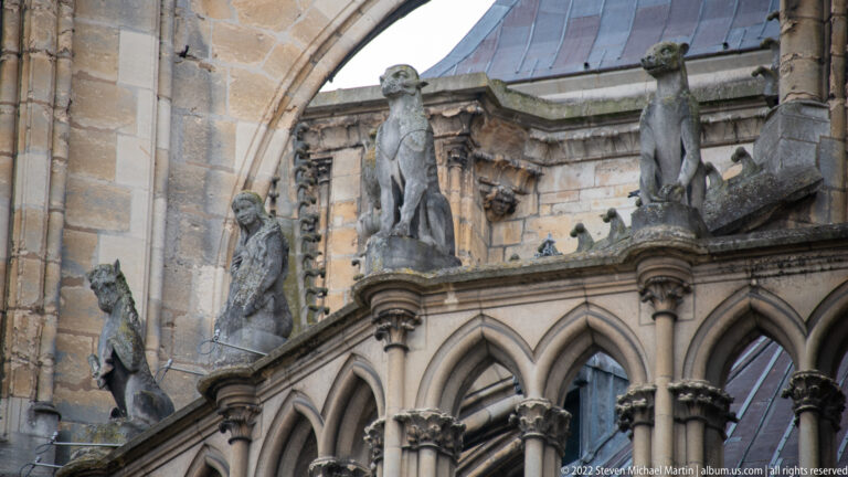 Several stone animal gargoyles project above pointed Gothic arcades on the exterior of Reims Cathedral.