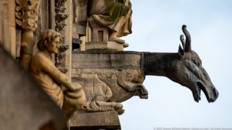Long-eared stone gargoyle with narrow snout projecting beside other cathedral sculptures.