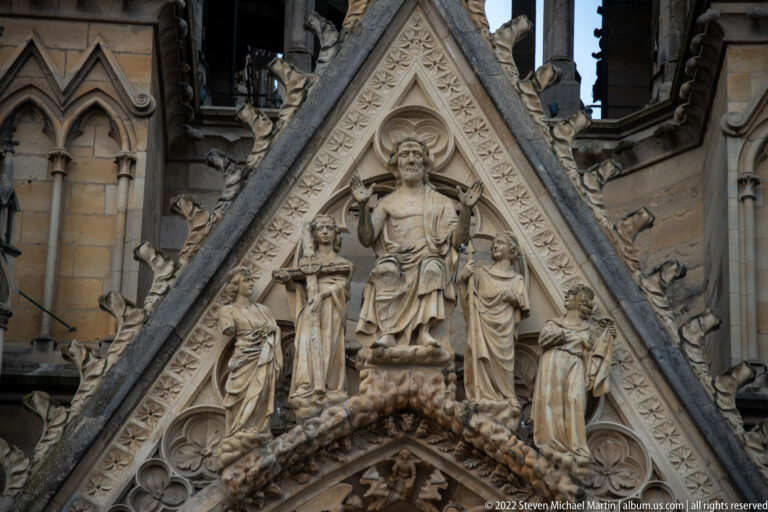 Seated haloed Christ surrounded by standing and kneeling figures within a carved triangular cathedral gable.