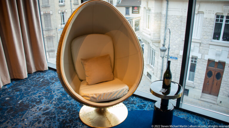 Cream egg chair beside a hotel window with a small table holding a bottle of Champagne.