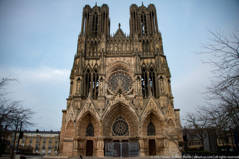 Daylight view of Reims Cathedral’s west façade with twin towers, central rose window, and three sculpted portals.