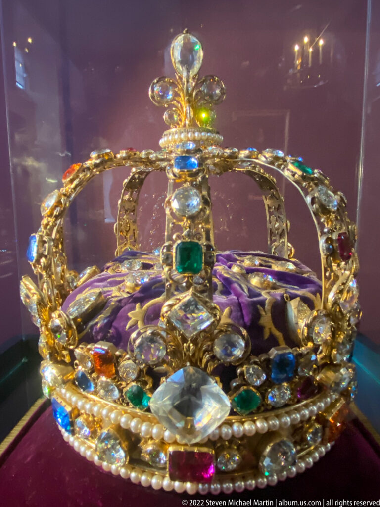 Jeweled royal crown with pearls, colored gemstones, arched bands, and purple fleur-de-lis lining.