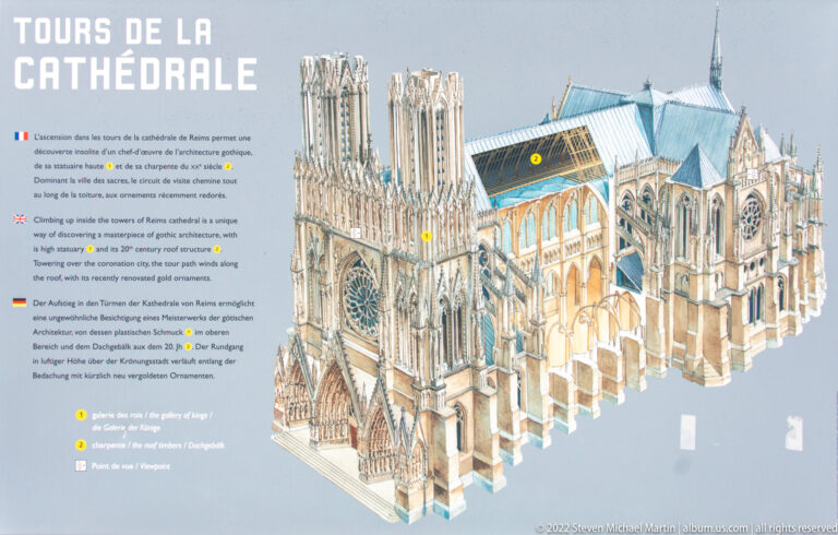 Museum panel with a cutaway model of Reims Cathedral and multilingual text marking locations used during French royal coronations.