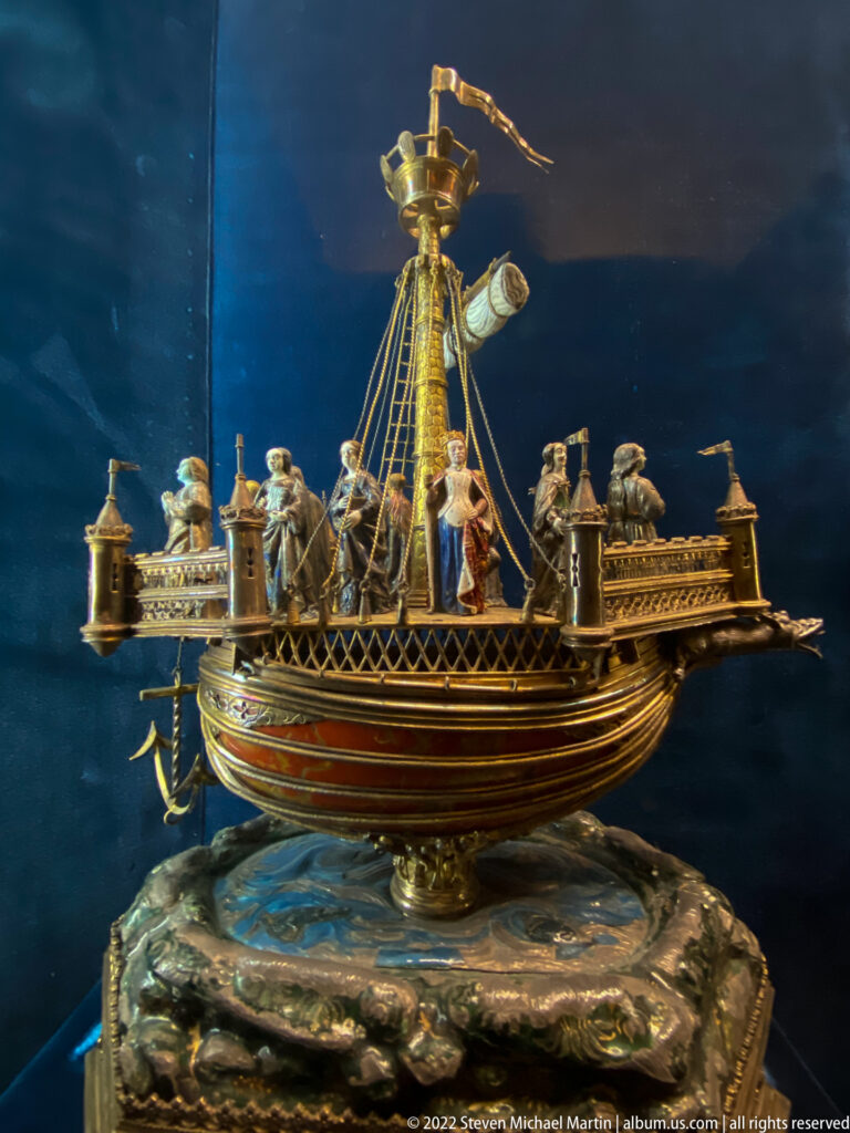 Gold-toned ship-shaped ceremonial vessel with mast, pennant, railings, and miniature figures on deck.