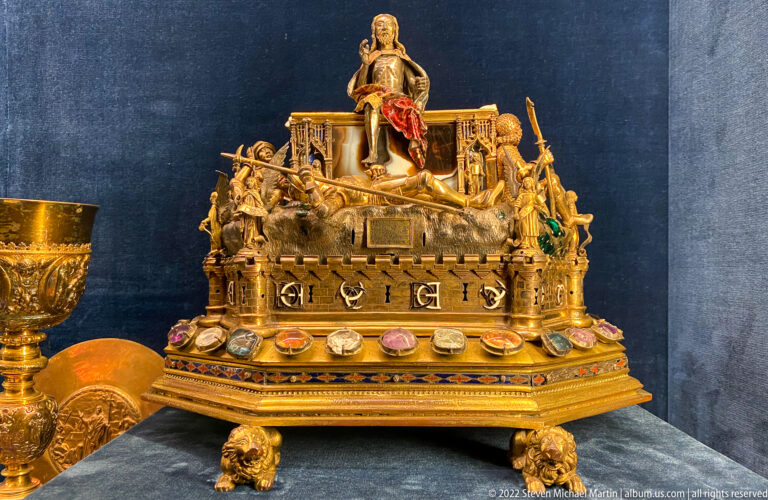Large gilded reliquary with miniature figures, gemstones, architectural details, and sculpted feet.