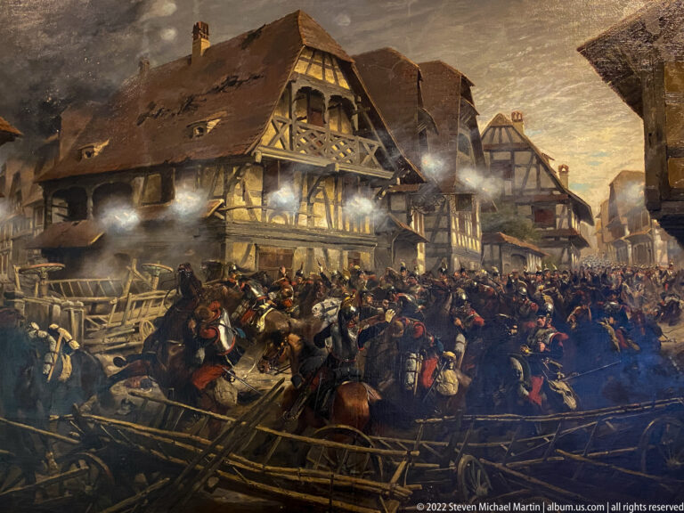 Historical battle painting with mounted troops, barricades, smoke, and timber-framed buildings in a crowded street.