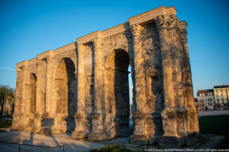 Roman Porte de Mars in Reims with three large arches, engaged columns, and weathered stonework in warm light.