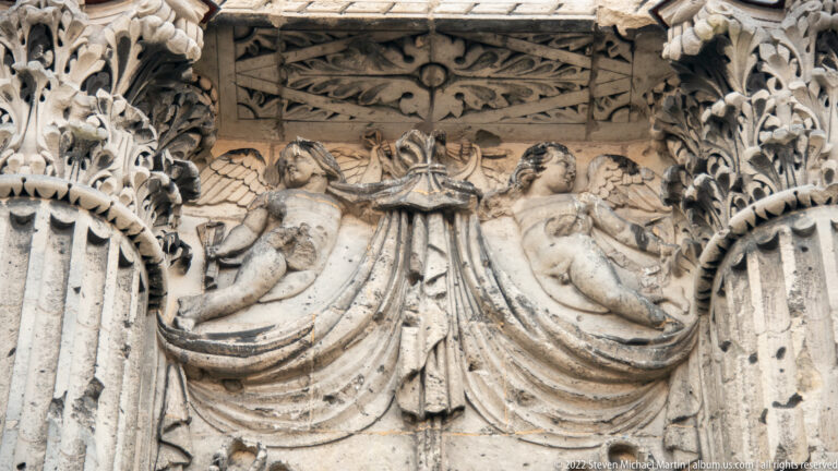 Weathered Roman relief with two reclining female figures flanking a central draped motif amid carved foliage and moldings.