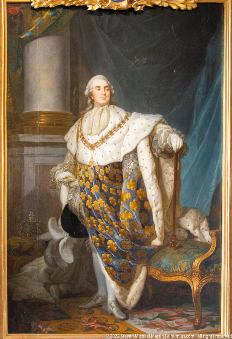 Standing French monarch in fleur-de-lis and ermine robes beside a ceremonial seat and draped interior.