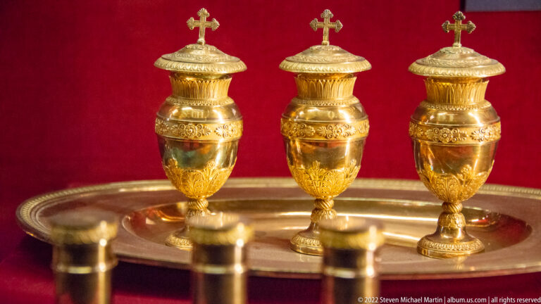 Three matching gilt covered vessels with cross finials arranged on a metal tray.
