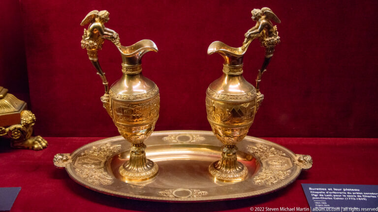 Two ornate handled ewers standing side by side on an oval decorated metal tray.