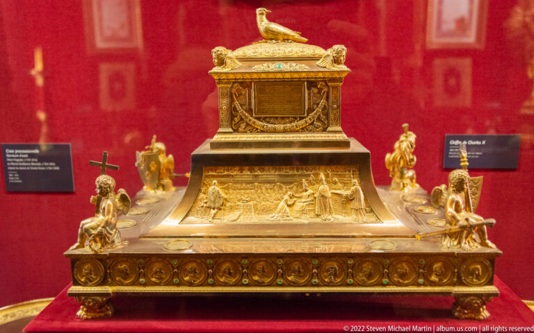 Large gilt reliquary-like casket on a sculptural base with figures and a bird finial.