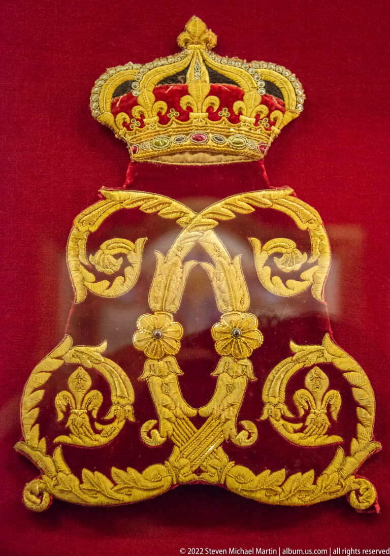 Crimson velvet textile embroidered in gold with a crown, large interlaced monogram, and scrolling motifs.