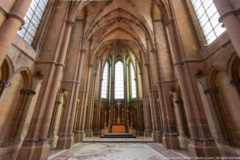 Gothic stone interior with pointed arches, rib vaults, tall windows, and an altar at the far end.