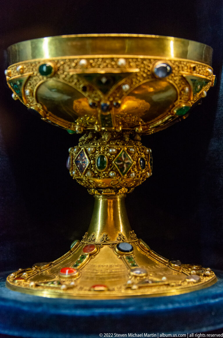 Low broad gold chalice with jeweled knop, decorated bowl, and wide gem-set foot.