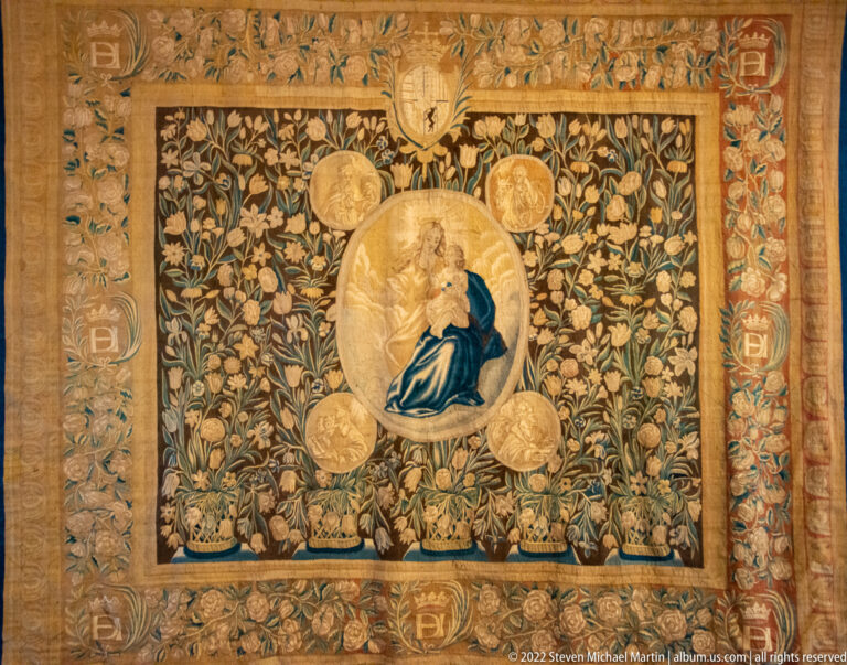 Floral tapestry with Virgin and Child in a central oval medallion, smaller roundels, and heraldic ornament.