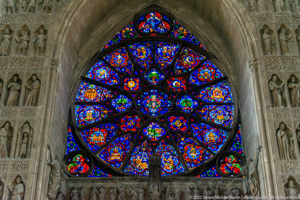 Large circular Gothic rose window with radiating tracery and vivid blue, red, and gold stained glass.