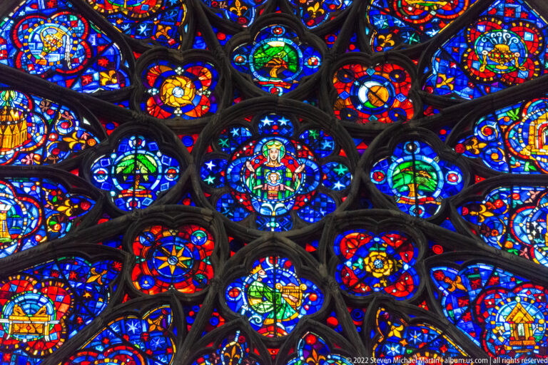 Close detail of a Gothic rose window with blue-dominant figural medallions and radiating stone tracery.