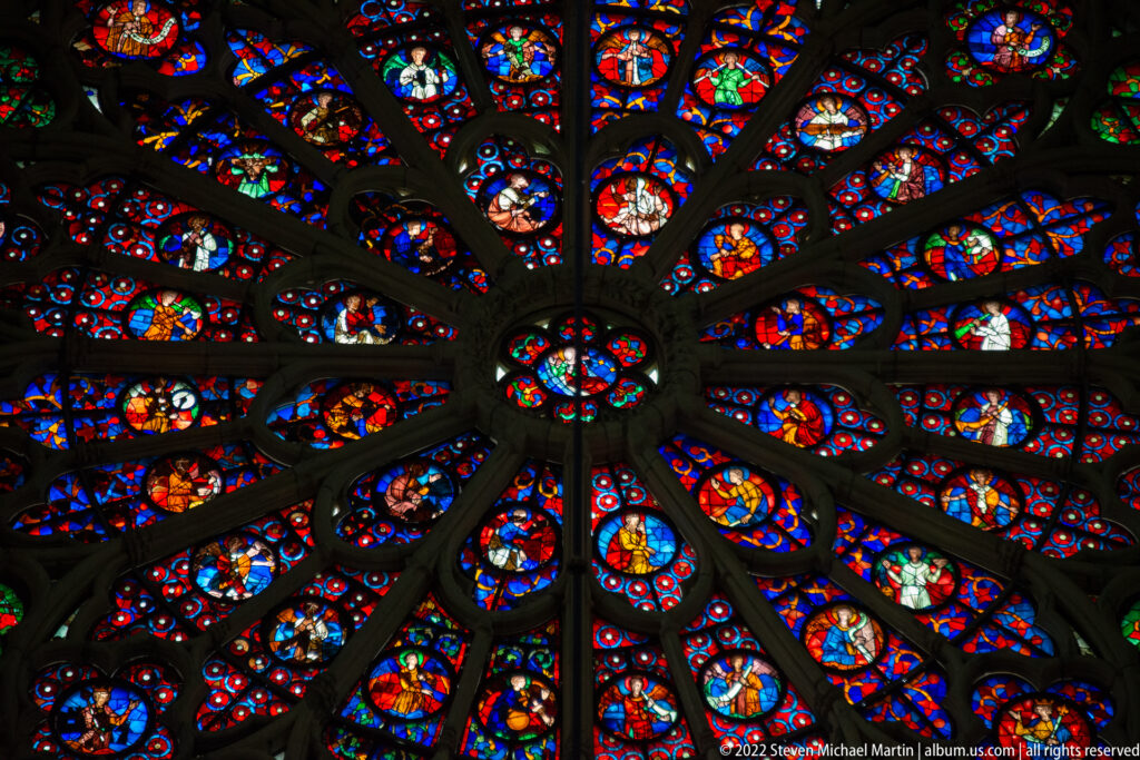 Upward view of a large stained-glass rose window, its dark radial tracery filled with multicolored glass.