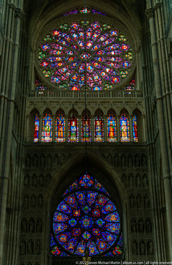 Interior elevation with two rose windows, a row of stained-glass lancets, and sculpted Gothic arcading.