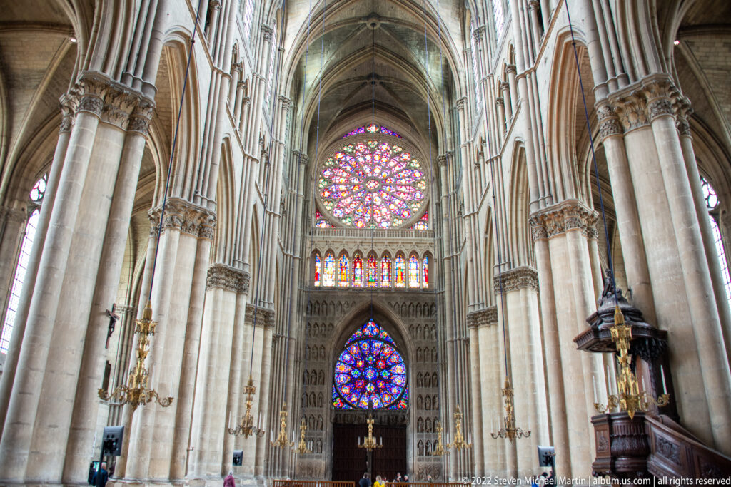Reims Cathedral nave framed by tall piers, with a rose window and lower stained glass at the far end.
