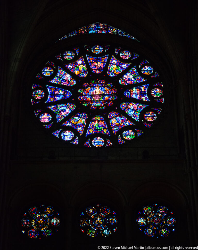 Large illuminated rose window above three smaller circular stained-glass windows in a dark cathedral interior.