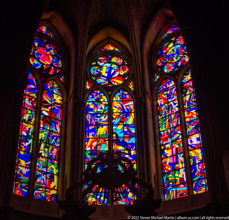 Modern abstract stained-glass lancets in vivid primary colors within Gothic stone tracery.