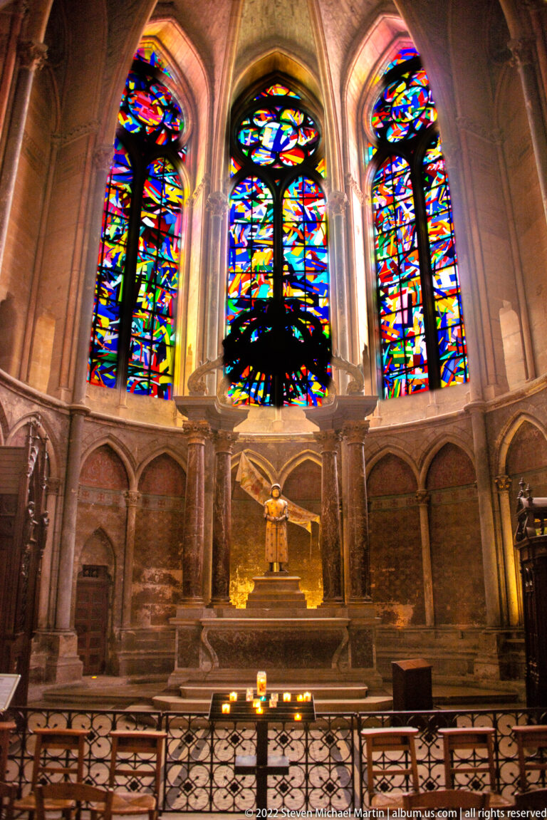 Side chapel in Reims Cathedral beneath vivid abstract stained-glass lancets and Gothic stone arches.
