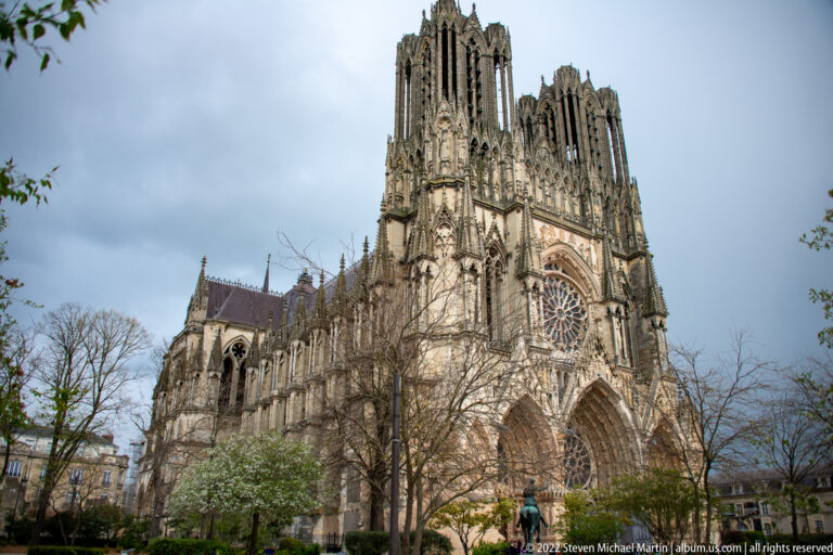 Oblique exterior view of Reims Cathedral showing twin west towers, rose window, nave, and flying buttresses.