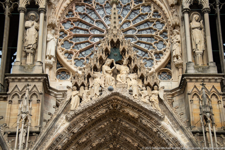 Sculpted Coronation of the Virgin group above a Reims Cathedral portal beneath the west rose window.