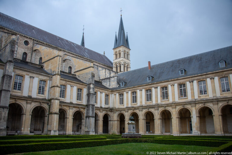 Arcaded Saint-Remi courtyard with formal hedges and a church tower rising beyond the surrounding roofs.