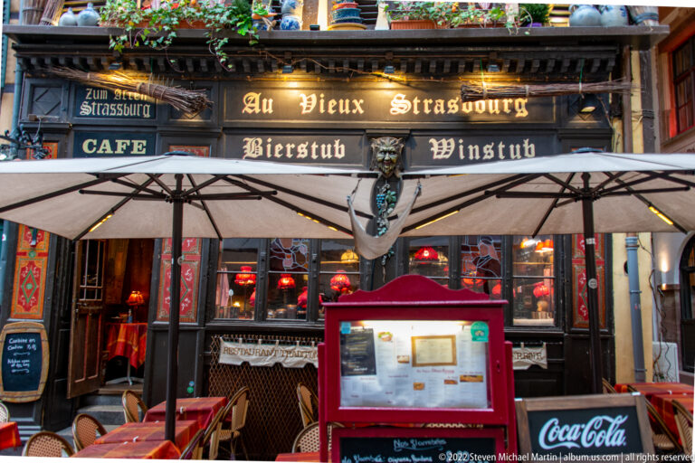 Au Vieux Strasbourg restaurant façade with winstub signage, red lamps, umbrellas, and a menu display.