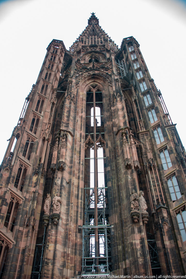 Upward view of Strasbourg Cathedral’s carved sandstone façade with Gothic tracery and a tall central scaffold.