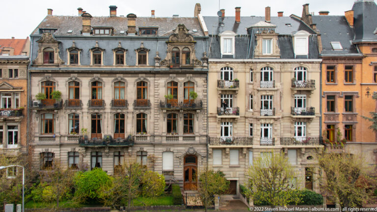 Ornate historic apartment façades with balconies, mansard roofs, dormers, and carved stone details line a Strasbourg street.