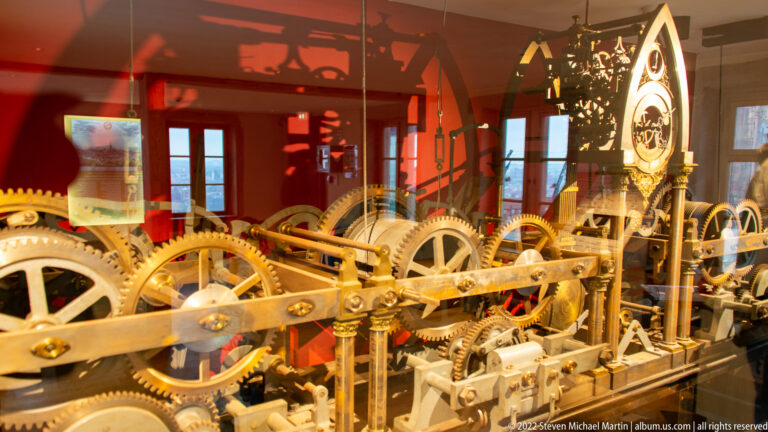 Brass gears, shafts, and toothed wheels of the Strasbourg Cathedral astronomical clock mechanism behind protective glass.