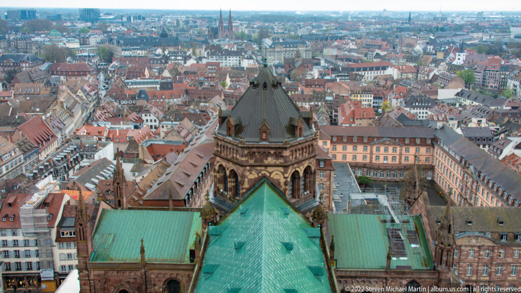 Green metal cathedral roof and octagonal Gothic tower seen from above, with Strasbourg rooftops spreading beyond.